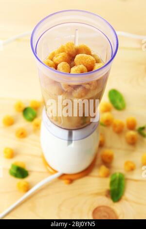 Lamponi gialli in tazza frullatore su tavolo di legno, primo piano Foto Stock