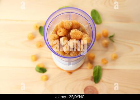 Lamponi gialli in tazza frullatore su tavolo di legno, primo piano Foto Stock