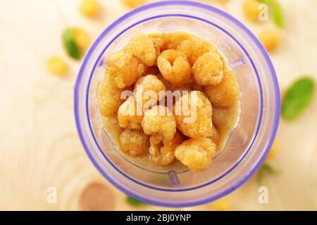 Lamponi gialli in tazza frullatore su tavolo di legno, primo piano Foto Stock
