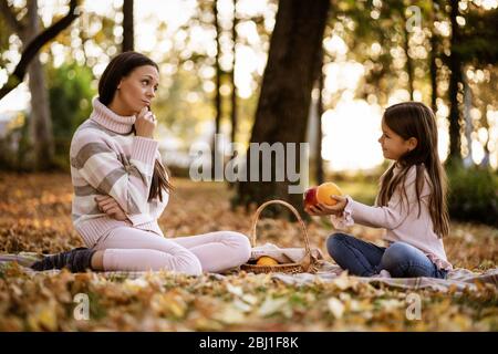 Madre e figlia che hanno pic-nic nel parco in autunno. Foto Stock