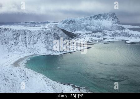 Vista dal monte Mannen sulla spiaggia di Haukland - Lofoten - in inverno. Nuvole tempestose su montagne coperte di neve. Spiaggia tranquilla e vista mare turchese da pe Foto Stock