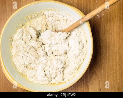 Mescolare l'impasto di pane di avena con farina di pane bianca forte e avena arrotolata in una terrina di miscelazione con un cucchiaio di legno Foto Stock