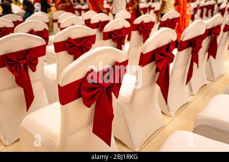 Sedie per matrimoni decorate con un arco rosso in una sala banchetti Foto Stock