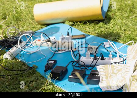 Molti cavi di prolunga elettrici, mazzo di gadget di ricarica, dispositivi elettronici, cavi capienti giacenti su tappeto erboso batterie di alimentazione, accumulato Foto Stock