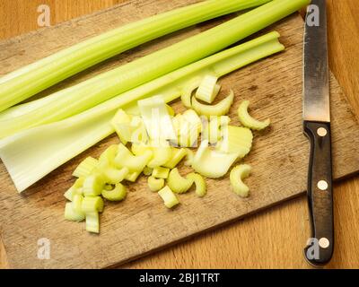 Tritare il sedano su un tagliere di legno su un tavolo da cucina Foto Stock