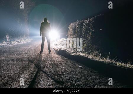 Una figura maschile sinistra in piedi davanti ad una macchina. Su una strada di campagna spooky in una notte nebbia. Foto Stock