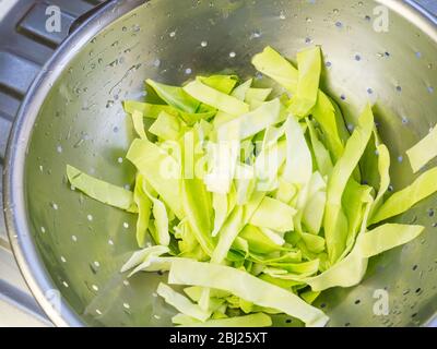 Lavate le fette di cavolo a punta in un colino di acciaio inossidabile su uno scolo da cucina Foto Stock