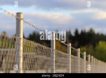 Vista ravvicinata su filo spinato su un campo con un bokeh morbido sullo sfondo Foto Stock