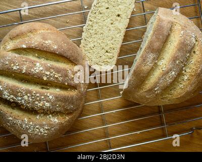 Pane appena sfornato con farina di pane bianco e farina di avena condita con avena arrotolata su una rastrelliera metallica Foto Stock