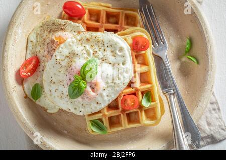 Deliziosi waffle fatti in casa con uova fritte e pomodori ciliegini Foto Stock