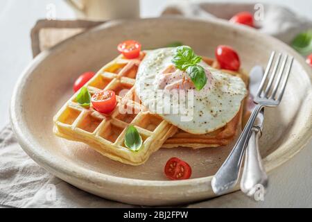 Primo piano di waffle fatti in casa con uova fritte e pomodori ciliegini Foto Stock