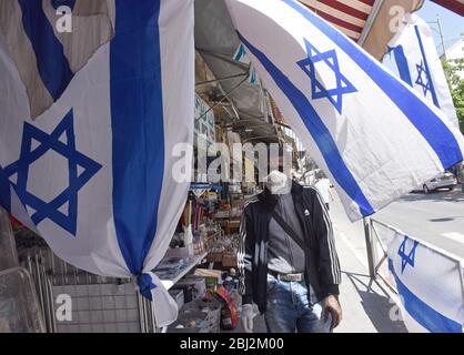 Gerusalemme, Israele. 28 Aprile 2020. Un israeliano indossa una maschera facciale obbligatoria, a causa della pandemia COVID-19, fuori da un negozio, che espone la bandiera nazionale, per il giorno della memoria e del giorno dell'indipendenza, a Gerusalemme, martedì 28 aprile 2020. Foto di Debbie Hill/UPI Credit: UPI/Alamy Live News Foto Stock