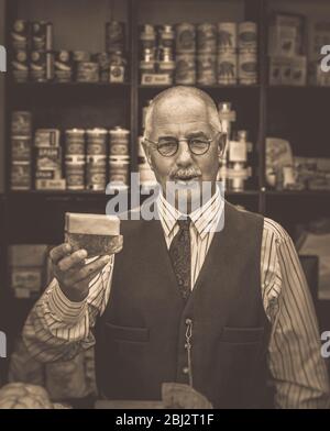 Vista frontale di Seppia dell'uomo degli anni '40 come negoziante d'epoca, drogheria, nel negozio della seconda Guerra Mondiale, evento estivo della seconda Guerra Mondiale degli anni '40. Foto Stock