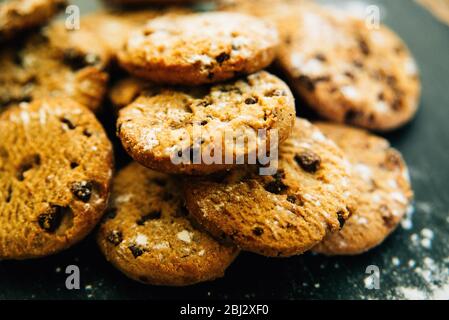 Primo piano di biscotti fatti in casa con scaglie di cioccolato e biscotti cosparsi di farina sull'ardesia Foto Stock