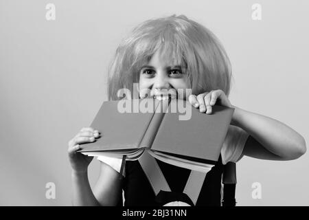 Ragazza morde Big Blue Book. Si torna a scuola e istruzione concetto. Pupilla in uniforme scolastica con parrucca rosa. School girl isolato su sfondo rosa. Foto Stock