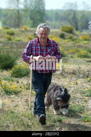 28 aprile 2020, Brandenburg, Dallgow-Döberitz: Shepherd Johann Nesges da Liedekahle (distretto Teltow-Fläming) cammina con il suo cane da pastore al mandria su un prato del paesaggio naturale di Sielmann nel Döberitzer Heide. Il contadino portò circa 900 pecore nella zona per la conservazione del paesaggio. Dalla metà di maggio, due grandi mandrie con un totale di circa 4000 pecore e capre si nutriranno sulla zona sul bordo occidentale di Berlino per la conservazione della natura e la biodiversità. A seconda della situazione del mangime, gli animali probabilmente rimangono fino alla fine dell'autunno. Foto: Soeren Stache/dpa-Zentralbild/dp Foto Stock