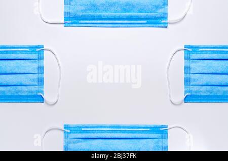 sui lati sono presenti quattro maschere blu per il viso su sfondo chiaro. al centro dell'immagine c'è spazio per la copia. sfondo medico. posa piatta Foto Stock