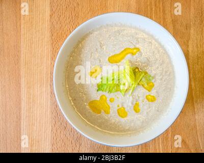 Una ciotola di zuppa di sedano ghiacciata a base di insalata Waldorf, condita con olio di colza e una guarnizione di foglie di sedano Foto Stock