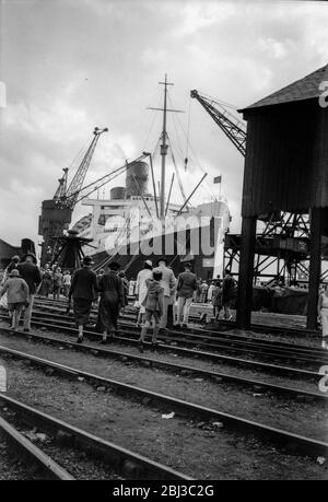 La linea Cunard-White Star transatlantico liner la RMS Queen Mary nel molo a Southampton come la gente attraversa le linee ferroviarie per vederlo, negli anni trenta Foto Stock