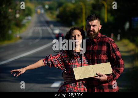 Coppia innamorata viaggiando con autostop, spazio copia. Uomo e donna cercano di fermare l'auto con cartello e gesto. Concetto di strada e di autostop. Coppia con facce stanche viaggio con arresto automatico. Foto Stock