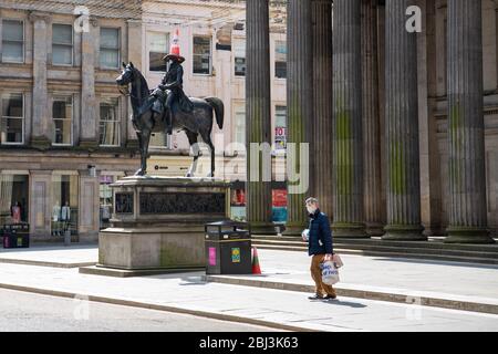 Glasgow, Scozia, Regno Unito. 28 Aprile 2020. Coronavirus Scotland UK: Uno shopper che indossa una maschera passa l'iconica statua del Duca di Wellington a Glasgow e indossa una maschera, come dice il governo scozzese che scozzese dovrebbe considerare di indossare coperture per il viso quando si visitano i negozi o si utilizzano i trasporti pubblici Credit: Kay Roxby/Alamy Live News Foto Stock
