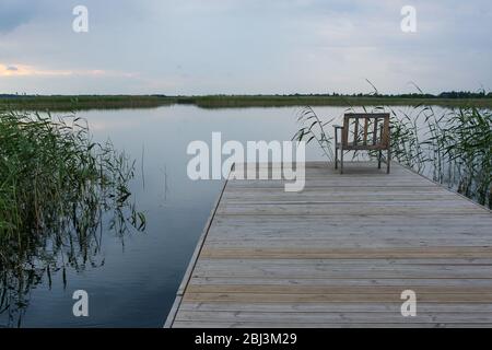 Una sedia su un ponte su un lago tranquillo Foto Stock
