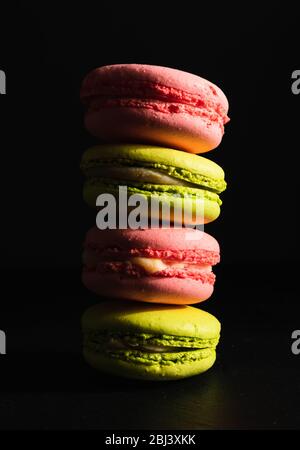 dolci concetto pubblicitario, dessert francese - macaroon rosa e pistacchio su sfondo nero, primo piano Foto Stock
