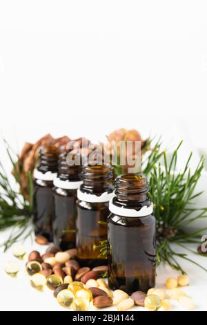 concetto di prodotto naturale, composizione di bottiglie di vetro con olio, cedro, capsule noci e malta su fondo bianco Foto Stock