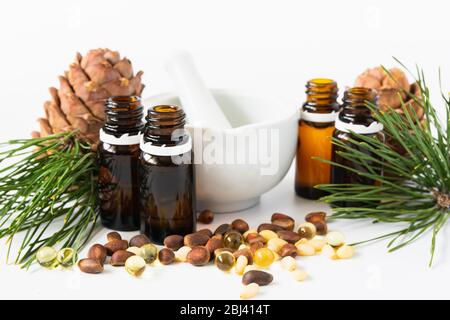 concetto di prodotto naturale, composizione di bottiglie di vetro con olio, cedro, capsule noci e malta su fondo bianco Foto Stock