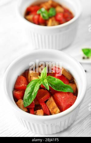 Gustosa ratatouille vegetariana a base di melanzane, squash, pomodori in ciotole su sfondo di tavolo in legno Foto Stock