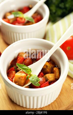 Gustosa ratatouille vegetariana a base di melanzane, squash, pomodori in ciotole su sfondo di tavolo in legno Foto Stock