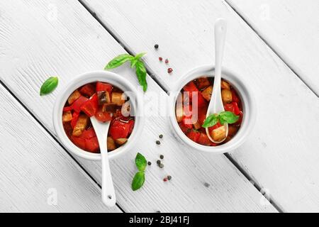 Gustosa ratatouille vegetariana a base di melanzane, squash, pomodori in ciotole su sfondo di tavolo in legno Foto Stock