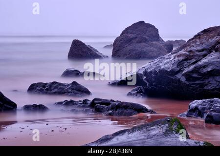 Onde al tramonto sulle rocce della spiaggia Praia de Arrifana. Trekking con Backpacker solo sulla Rota Vicentina e il sentiero dei pescatori in Algarve, Portogallo Foto Stock
