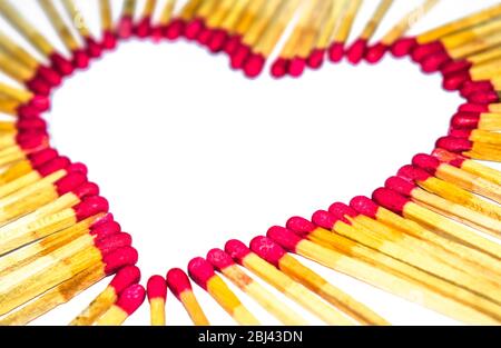 Forma a cuore realizzata con bastoncini di legno infiammabile di colore rosso prima di uno sfondo isolato bianco Foto Stock