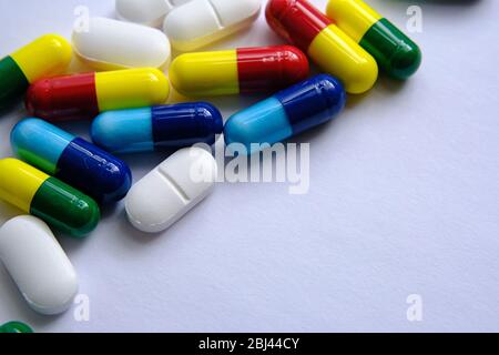 Pile di pillole di diversi colori: Blu, giallo, rosso e bianco) poste sopra la carta bianca. Illustrativa per i soggetti medici, sanitari e di altro tipo. Ma Foto Stock