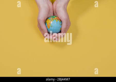 Globo in mano su sfondo giallo con spazio per la copia. Il mondo intero è nelle vostre mani. Proteggere il mondo dalla guerra e dal disastro. Problemi di ecologia. Foto Stock