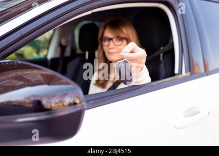 Scatto di donna sicura che tiene una chiave dell'automobile nella sua mano mentre siede nella sua automobile. L'attenzione è rivolta alla chiave della vettura. Foto Stock