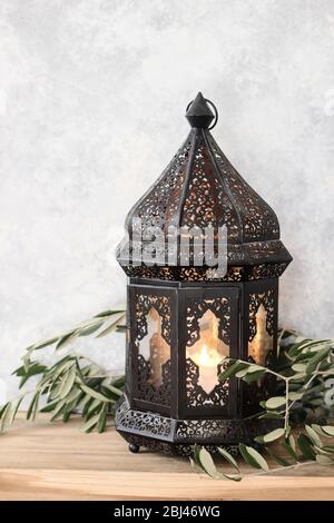 Lanterna marocchina decorativa scura. Foglie di ulivo verde, rami su vecchio tavolo di legno. Messa a fuoco selettiva, sfondo muro shabby. Biglietto d'auguri per i musulmani Foto Stock