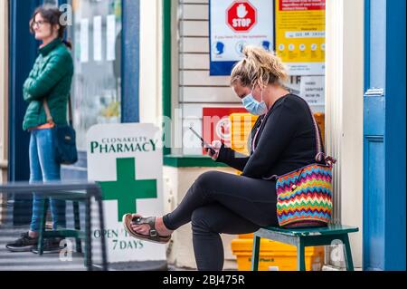 Clonakilty, West Cork, Irlanda. 28 Aprile 2020. Una donna si accoda per entrare nella Clonakilty Pharmacy indossando una maschera facciale per proteggersi da Covid-19. Credit: AG News/Alamy Live News Foto Stock