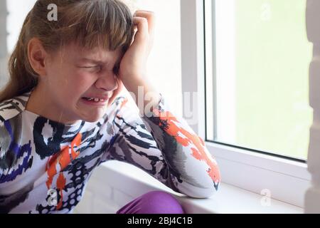 Ragazza teen che piange molto mentre si siede vicino alla finestra in camera, primo piano Foto Stock