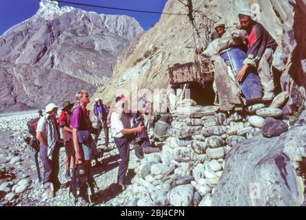 Pakistan, zone settentrionali delle montagne di Karakoram. Un gruppo europeo di trekking condivide il compito comune di caricare la scatola Jola per aiutare l'attraversamento del fiume Braldu alla testa della gola di Braldu. La Jola è stata sostituita da un ponte di sospensione che rende l'operazione più facile e sicura Foto Stock