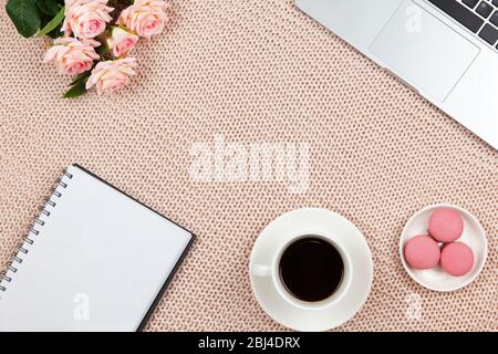 Lavoro da casa concetto. Moderno spazio di lavoro femminile, vista dall'alto. Laptop, caffè, torte, rose, taccuino su coperta a maglia, spazio di copia, piatto lay. Deskto Foto Stock