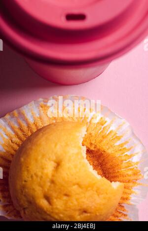 Vista dall'alto di un muffin e di una tazza di caffè. Parzialmente mangiato muffin su un tavolo rosa. Colazione con muffin e caffè Foto Stock