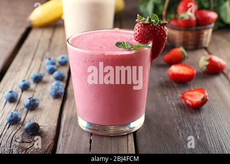 Bicchieri di frullato fresco freddo con frutta e frutti di bosco su fondo in legno Foto Stock