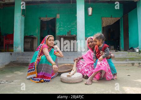 Donna indiana che tiene un bambino e macina la farina in un villaggio Foto Stock