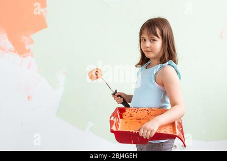 Riparazione in appartamento. Ragazza felice bambino dipinge il muro con vernice arancione. Concetto di rinnovo e riarredo. Foto Stock