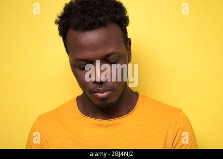 Giovane afroamericano guardando giù con colpevole espressione confusa Foto Stock