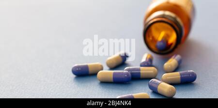 Capsule di medicinale sparse da un flacone di vetro su sfondo blu. Vista primo piano delle pillole di farmacia. Trattamento medico, concetto di salute Foto Stock