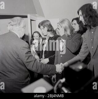1970, storico, visto da dietro, politico laburista e primo ministro, Harold Wilson in una stanza che scuote le mani con alcuni sostenitori maschi a pelo lungo, Londra, Inghilterra, Regno Unito. Foto Stock