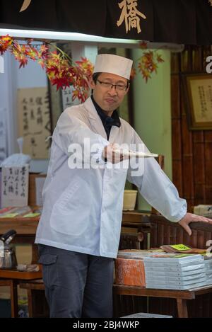 Uno chef offre assaggi di vari biscotti e gnocchi di tè ai turisti e ai visitatori in via Matsubara Dori a Kyoto Giappone. Foto Stock